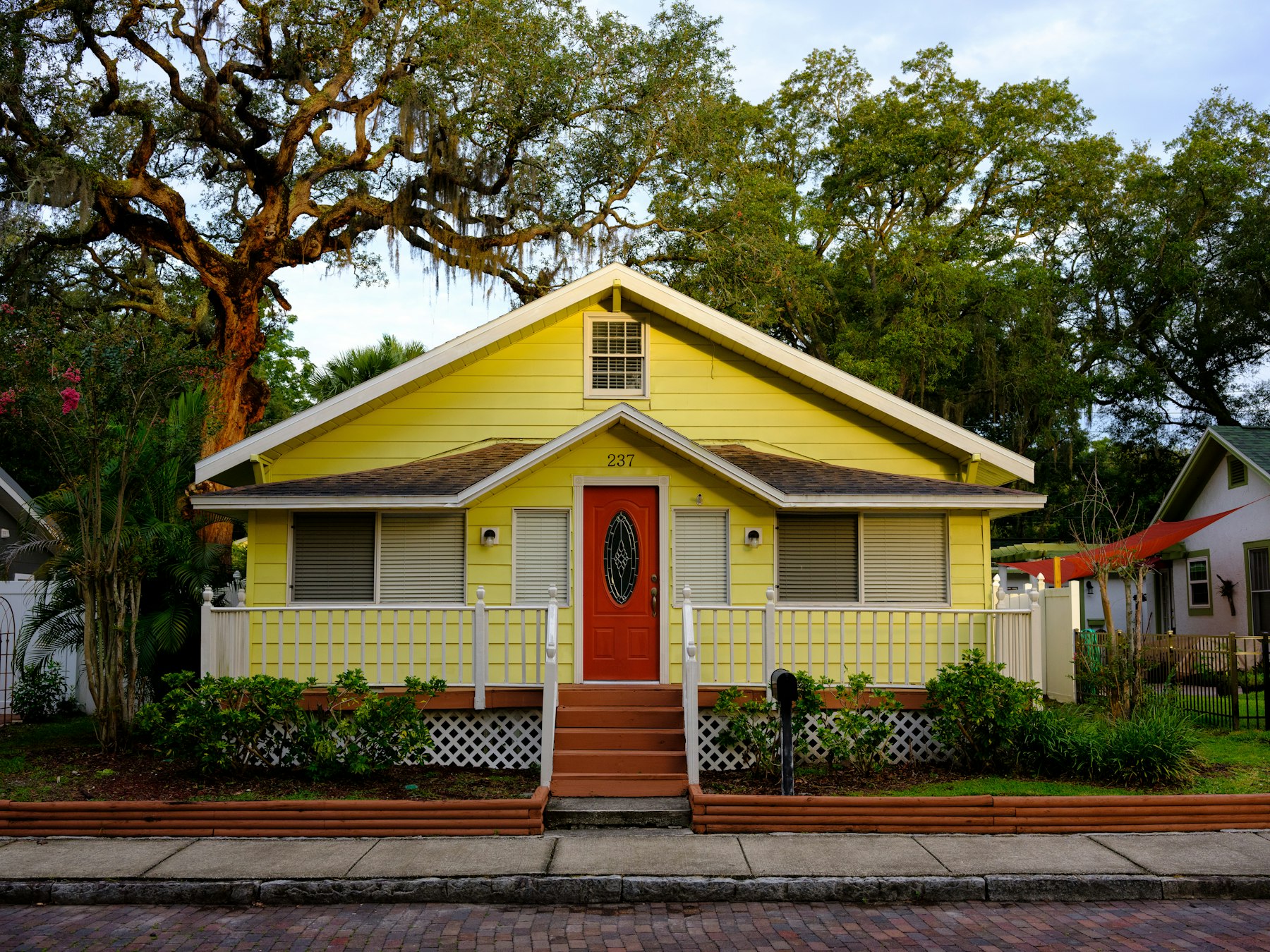 Yellow Florida cottage with a red front door under oak trees